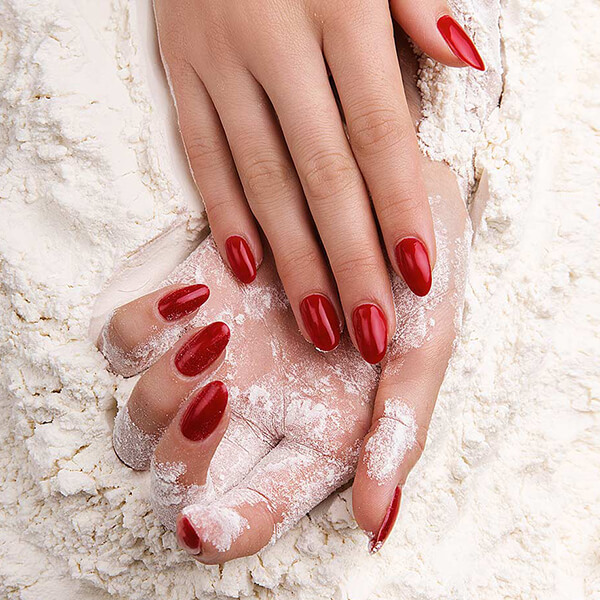 Glossy red almond manicure on a light textured background